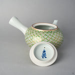 Underside of the Kyoto ware teapot lid, marked with a blue potter's signature, set before the open teapot body covered in a gold and green shippo pattern.
