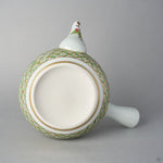 Underside of the Kyoto ware teapot body, unglazed foot ring bordered by gold bands, with the gold and green shippo pattern and the nandina-painted spout rising behind.