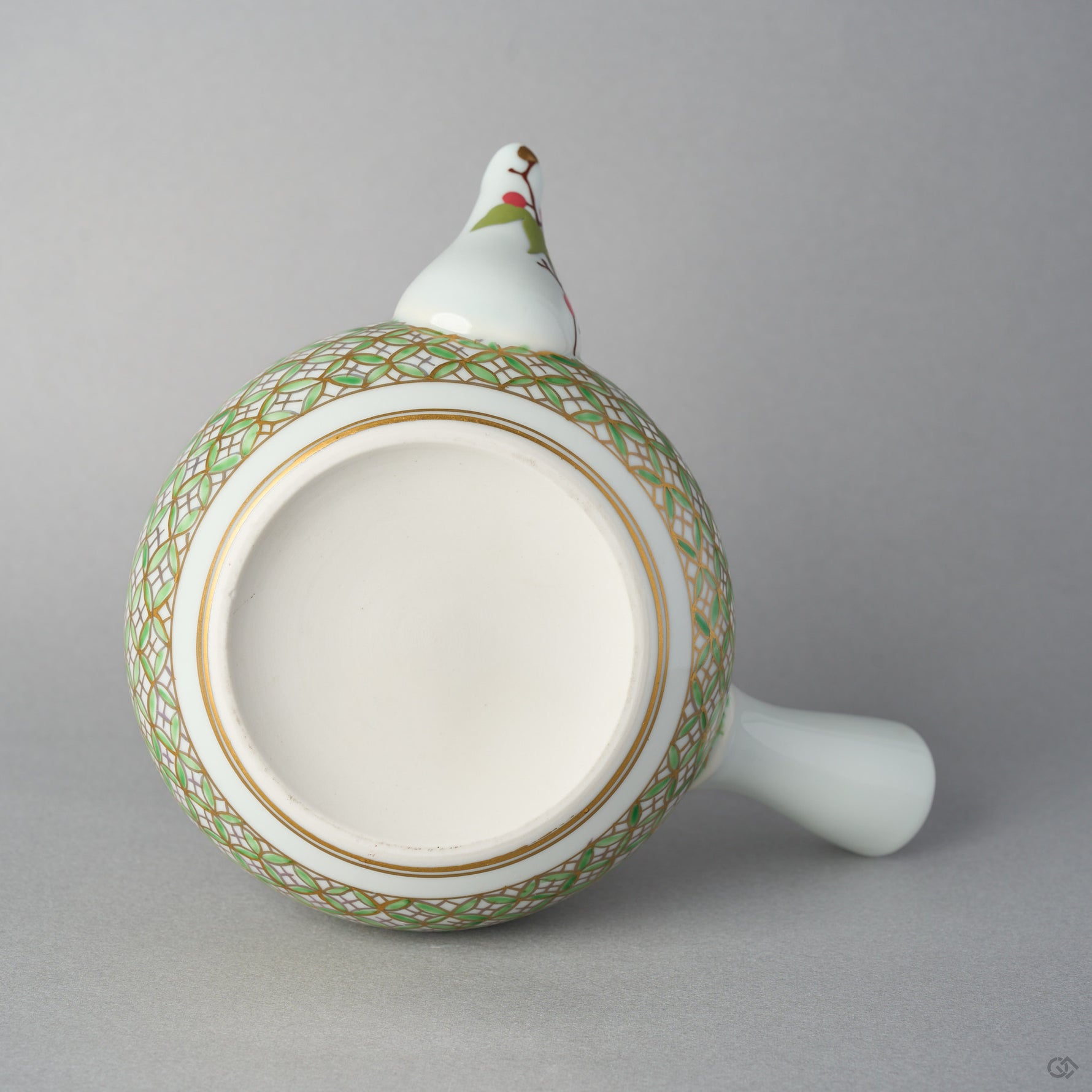 Underside of the Kyoto ware teapot body, unglazed foot ring bordered by gold bands, with the gold and green shippo pattern and the nandina-painted spout rising behind.
