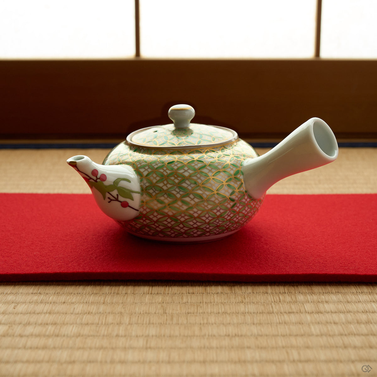 Kintsugi Kyoto ware teapot on a red felt runner over tatami, gold and green shippo pattern across the porcelain body and a nandina branch painted on the restored spout.