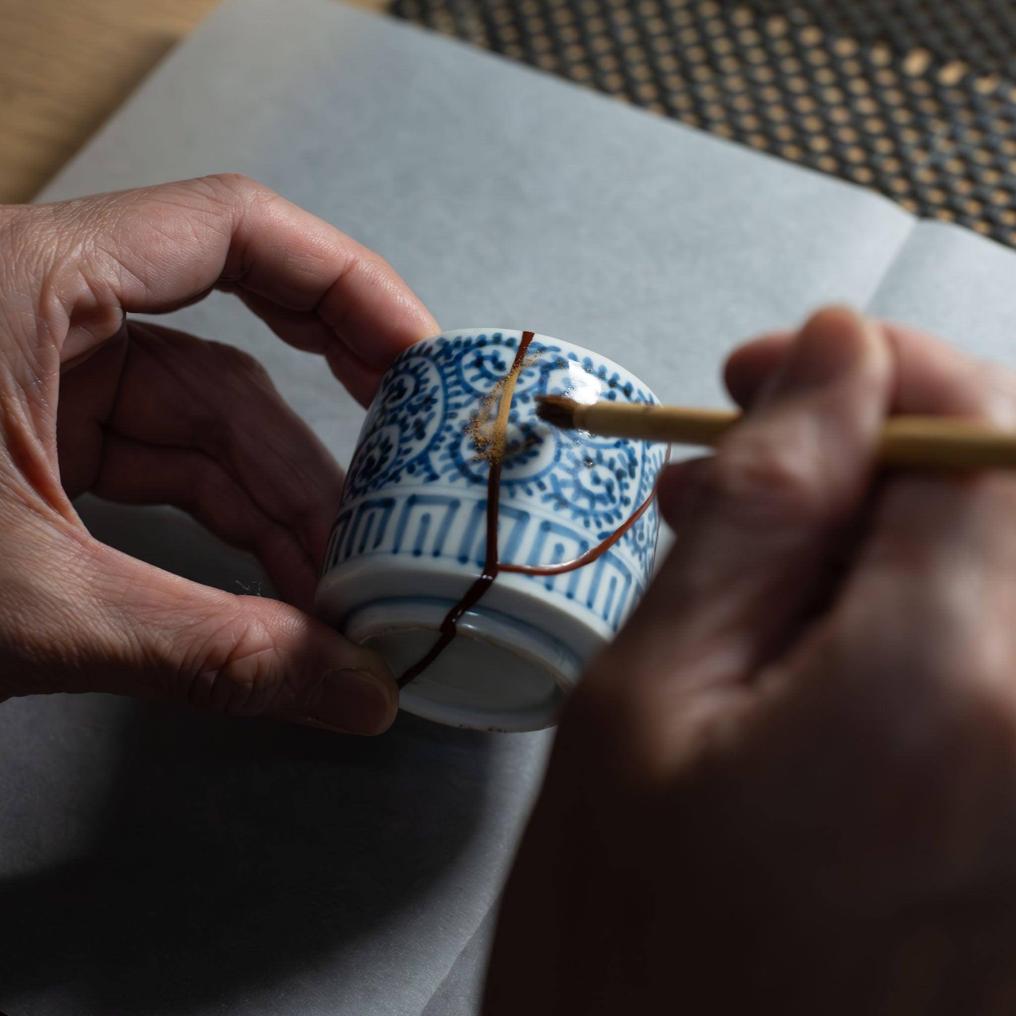 Urushi artist applying 24K gold powder by hand to the kintsugi seam of a sometsuke (blue-and-white) porcelain piece — The Kintsugi Labo JAPAN